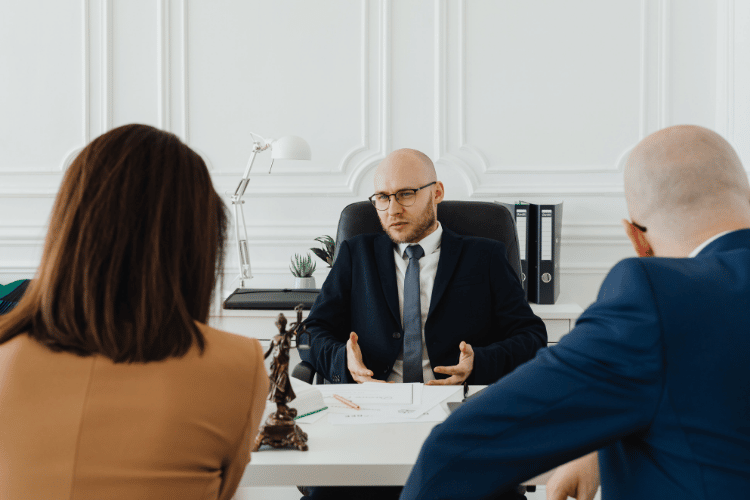 Is Hiring a Lawyer After a Car Accident Worth It? 4 Man in a suit sitting behind a desk speaking to a woman and another man. Getting a Lawyer for a Car Accident