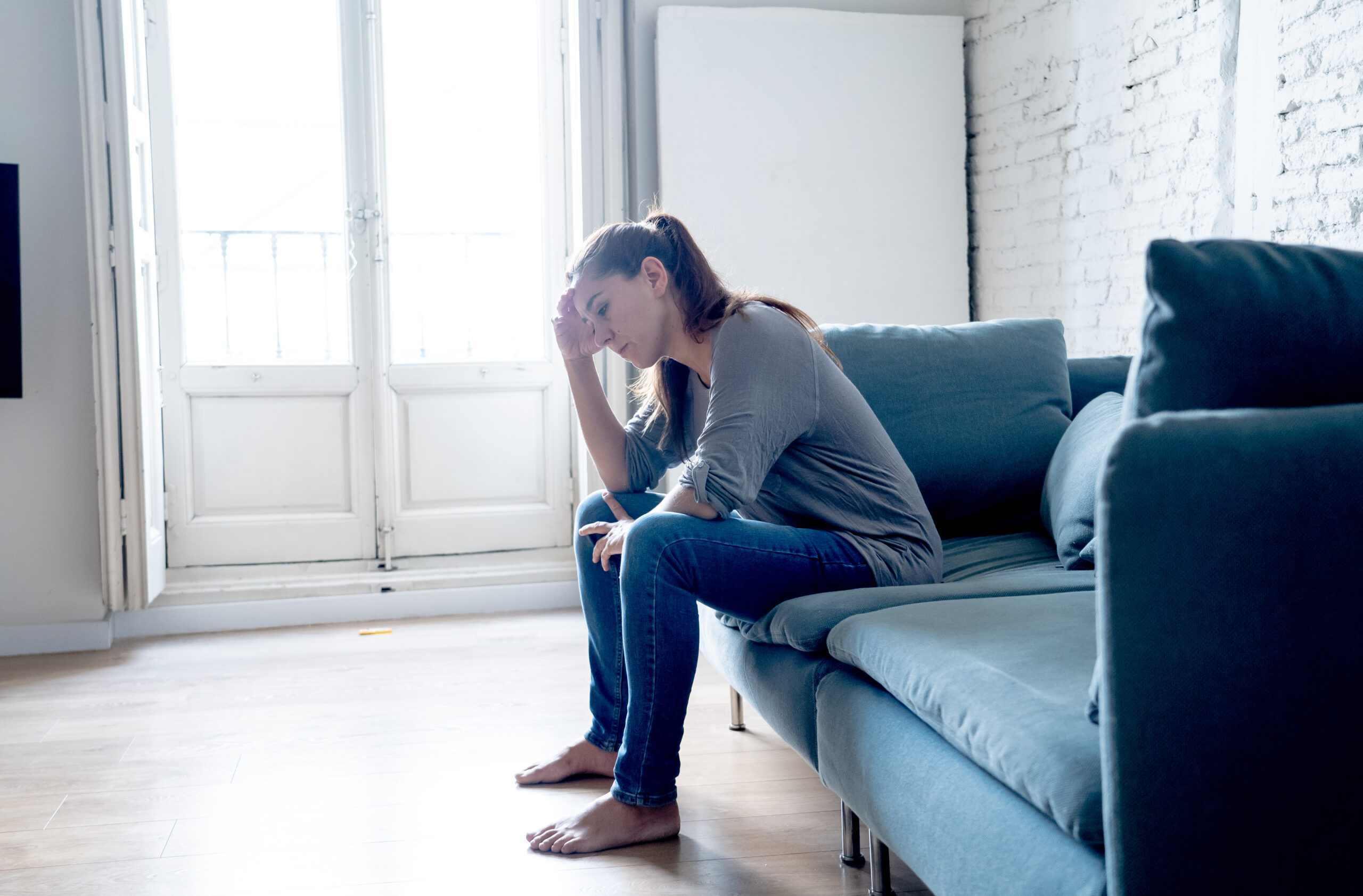 Joven y atractiva mujer latina tumbada en el sofá de la sala de casa sintiéndose triste, cansada y preocupada por sufrir depresión en la salud mental, problemas y concepto de corazón roto. Costo emocional de lesiones personales
