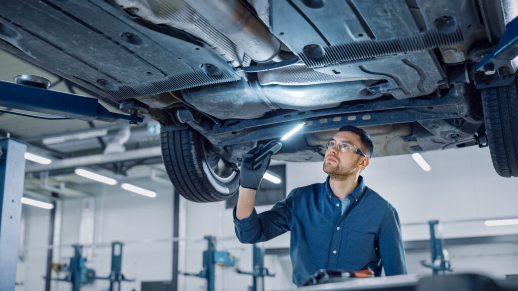 Tips to Maintain a Car That is Rarely Driven 4 Handsome Professional Car Mechanic is Investigating Rust Under a Vehicle on a Lift in Service. Repairman is Using a LED lamp and Walks Towards. Specialist is Wearing Safety Glasses. Modern Workshop.