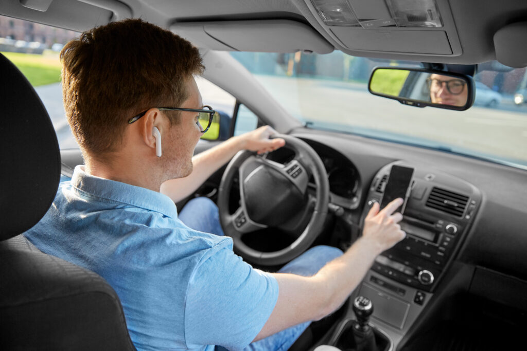 Man driving car and using GPS on smartphone. Transport, vehicle and people concept - man or driver with wireless earphones driving car and using GPS navigator on smartphone